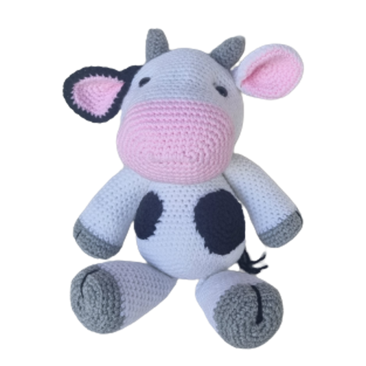 A crochet plush toy shaped and designed to look like a cow, with a predominantly white body, black spots, and a pink nose and mouth.
