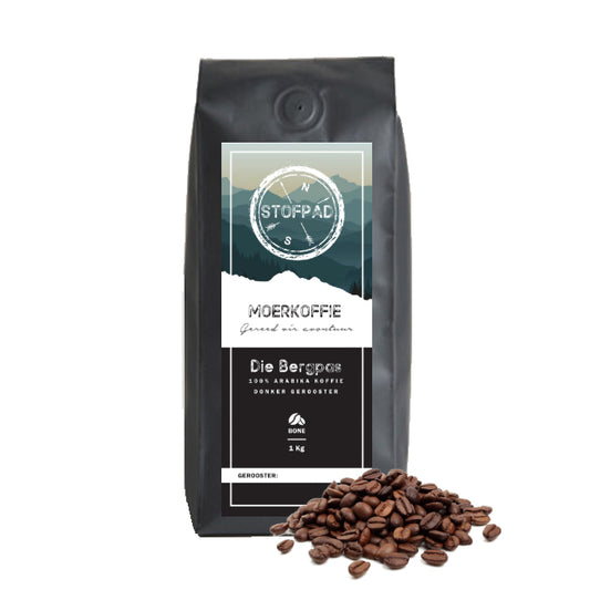 A pack of Die Bergpas Moerkoffie coffee beans with a dark roast label, indicating a strong body and caramel flavors. The beans are displayed in front of the packaging.