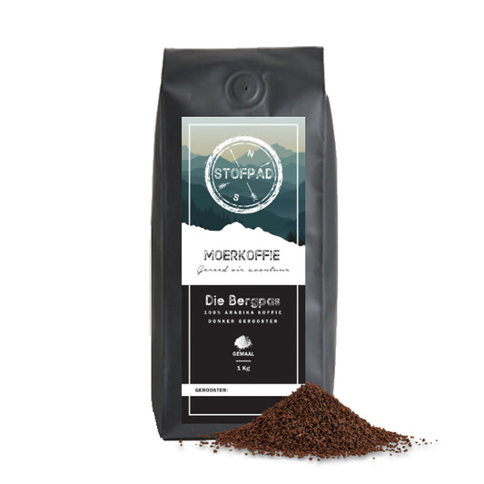 A pack of Die Bergpas Moerkoffie coffee beans with a dark roast label, indicating a strong body and caramel flavors. Heap of ground Coffee are displayed in front of the packaging.