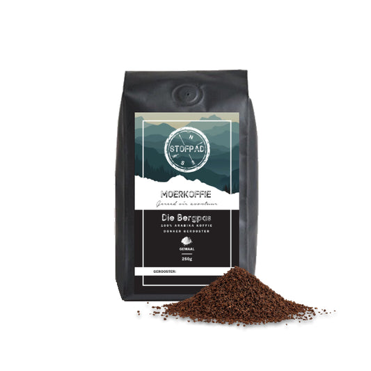 A bag of Die Bergpas Moerkoffie ground coffee with a small pile of coffee grounds in front of it, against a white background.