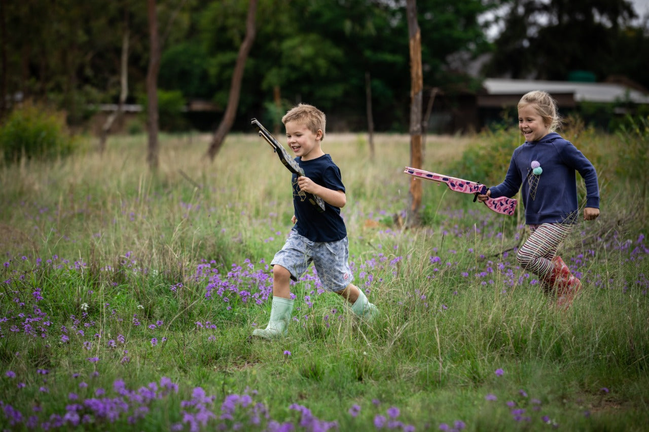 Boy and Girl running in a veld playing with Toy Guns